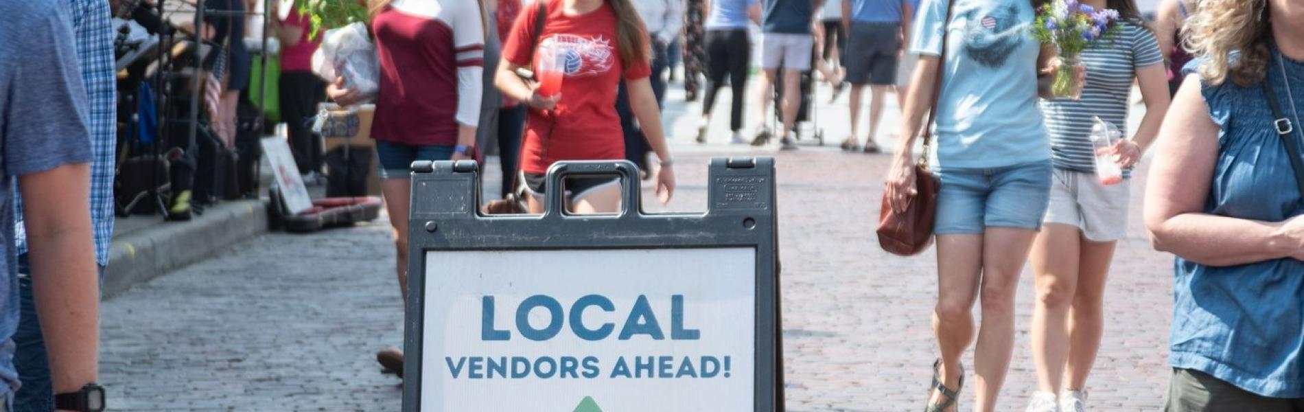 Picture of the Hendersonville Farmers Market with customers and a local vendor ahead sign