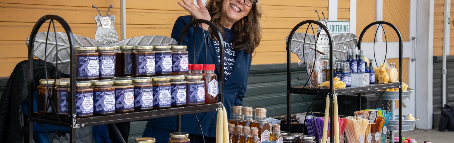 honey vendorwith jars of honey waving at the camera