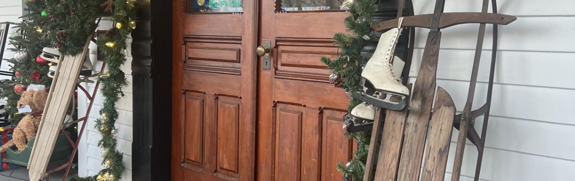 Entryway of a historic inn decorated with garland, reindeer, and a wooden sleigh.