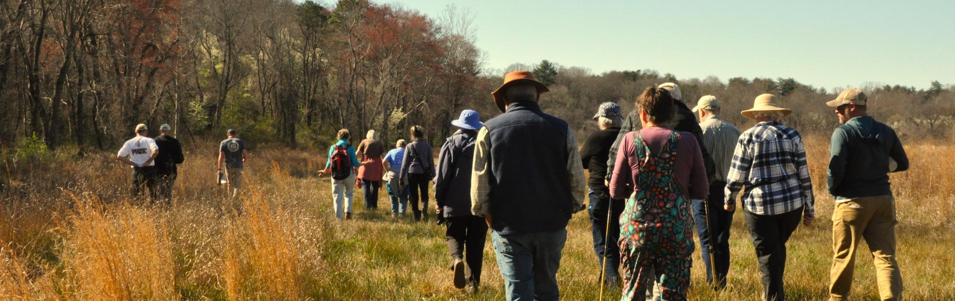 A large group of people walking outside in a field on a guided tour.