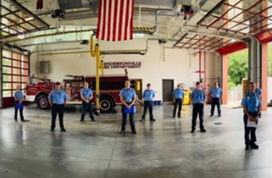 photo of 14 firefighters standing in the station bays in front of a fire truck with american flag hanging from the ceiling