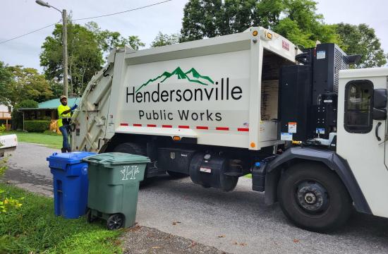 Environmental Service worker riding on the back of a Hendersonville Public Works Garbage truck