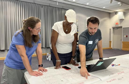 3 people at a history event pointing at historic maps