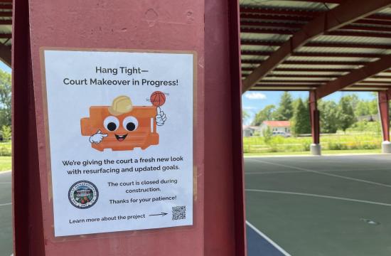 Sign saying basketball court is closed for construction with a cartoon barricade wearing a construction hat