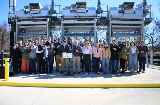 Group of people standing in front of a large water intake holding cups of water
