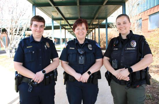 3 female officers smiling and wearing uniforms and badges. The officer in the center is the mother of the other two officers.