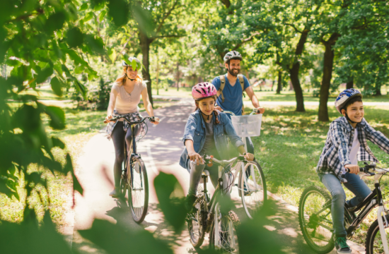 Family of 4 riding bikes in a park wearing bike helments