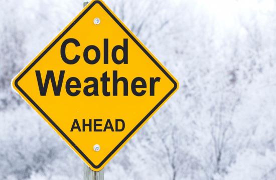 Sign saying cold weather ahead in front of a winter scene