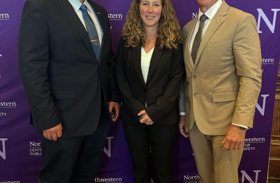 Three people stand in formal attire, smiling, in front of a purple Northwestern University backdrop.