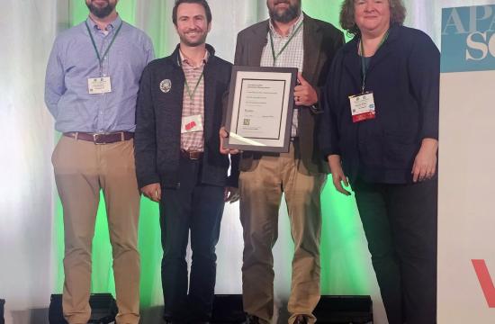 Four people stand and smile, holding an award plaque.