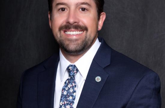 A man in a dark blue suit is smiling.