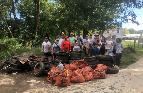 Picture of 17 individuals standing outside, with numerous bags of trash, tires, and other litter.