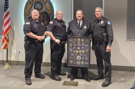 Four men in uniform, one holding a frame displaying various police badges.