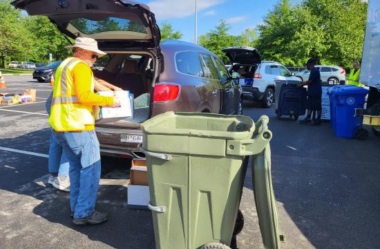 A person is dumping a box of documents into a trash can for shredding.