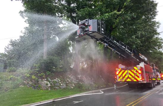 Red fire truck with the ladder raised, spraying water across a closed street.
