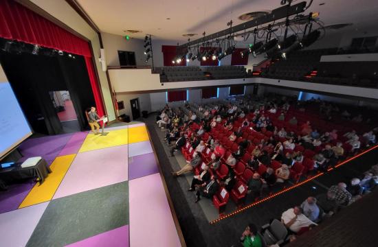 Hendersonville High School auditorium with housing expert speaking onstage and more than 100 people in the auditorium seats