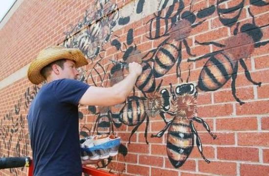 muralist painting bees on a brick wall