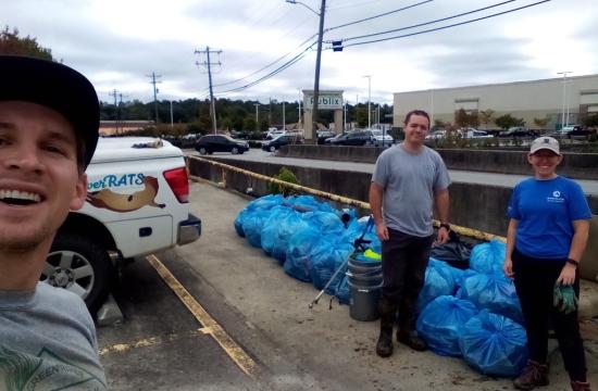 Stormwater staff and volunteers collecting trash from stream. Numerous blue garbage bags in background.