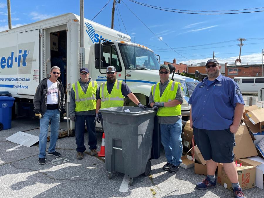 5 guys standing next to a trash can and shred truck