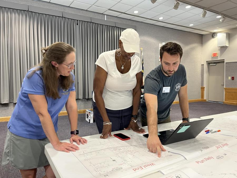 3 people at a history event pointing at historic maps