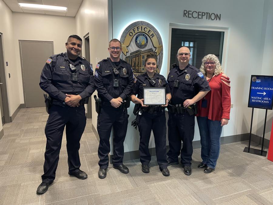 Four officers in uniform and one civilian stand together smiling, holding a certificate.