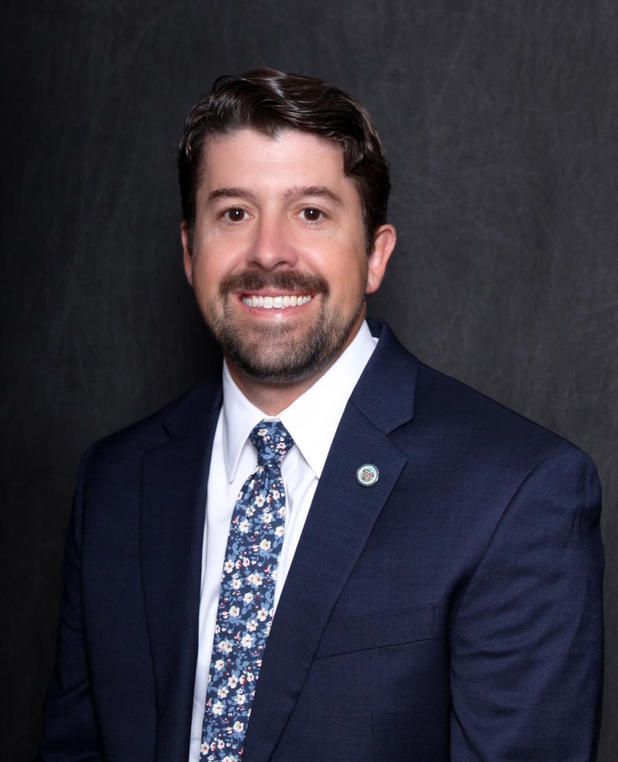 A man in a dark blue suit is smiling.