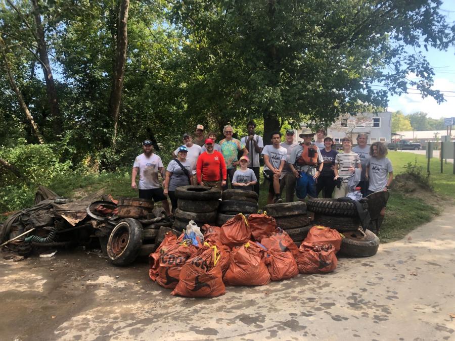 Picture of 17 individuals standing outside, with numerous bags of trash, tires, and other litter.