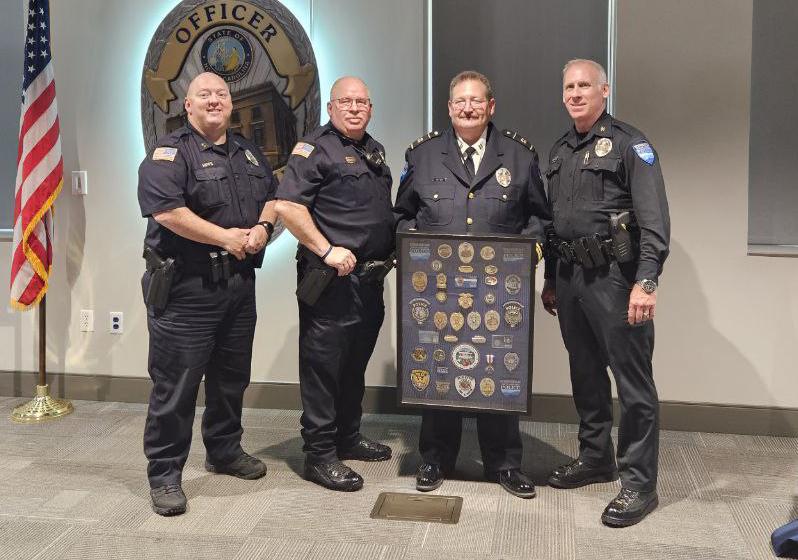 Four men in uniform, one holding a frame displaying various police badges.
