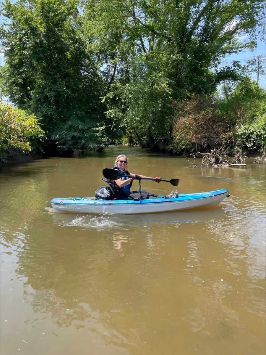 Person in a blue kayak holding a paddle, in a creek. 