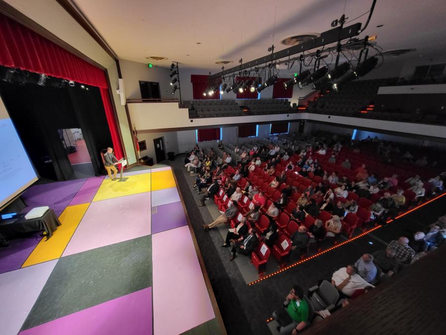 Hendersonville High School auditorium with housing expert speaking onstage and more than 100 people in the auditorium seats