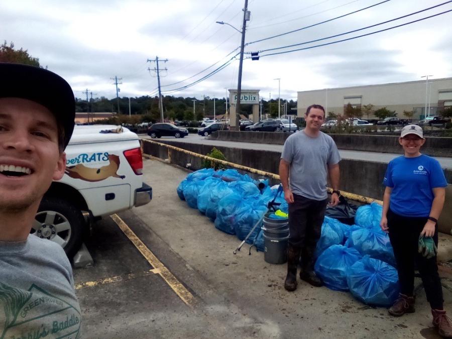 Stormwater staff and volunteers collecting trash from stream. Numerous blue garbage bags in background.