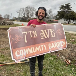 Past community member of garden, Tae Brown holding the original sign for the community garden