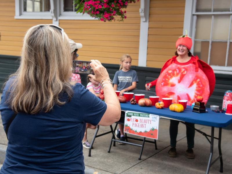 a women in a in a tomato costume getting her picture taken while annoying the winner of a tomato beauty pageant 