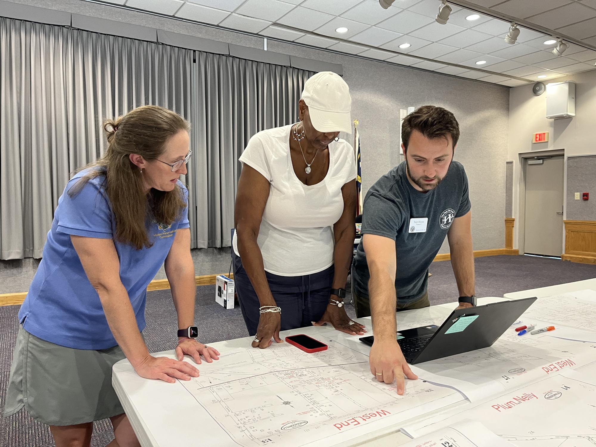 3 people at a history event pointing at historic maps