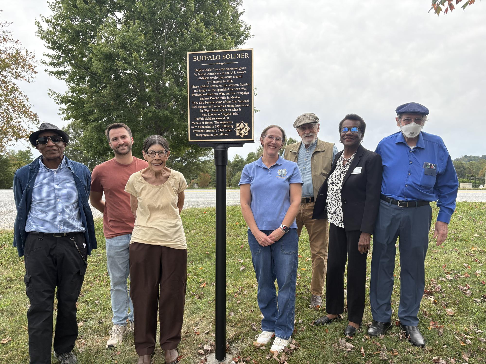 Group of people in a cemetery standing next to a historic marker