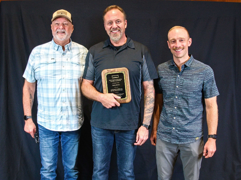 3 men smiling with one holding an award