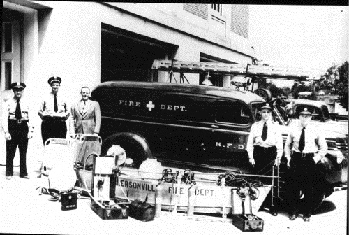 black and white photo of old fire department, truck, and crew. 5 men in front of truck behind their equipment 