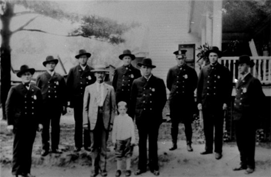 8 men in black uniforms, 1 man in a light colored suit, and a child