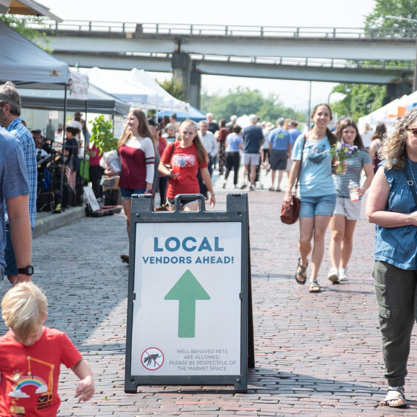 A crowed of people walking on the street at a Farmers Market 