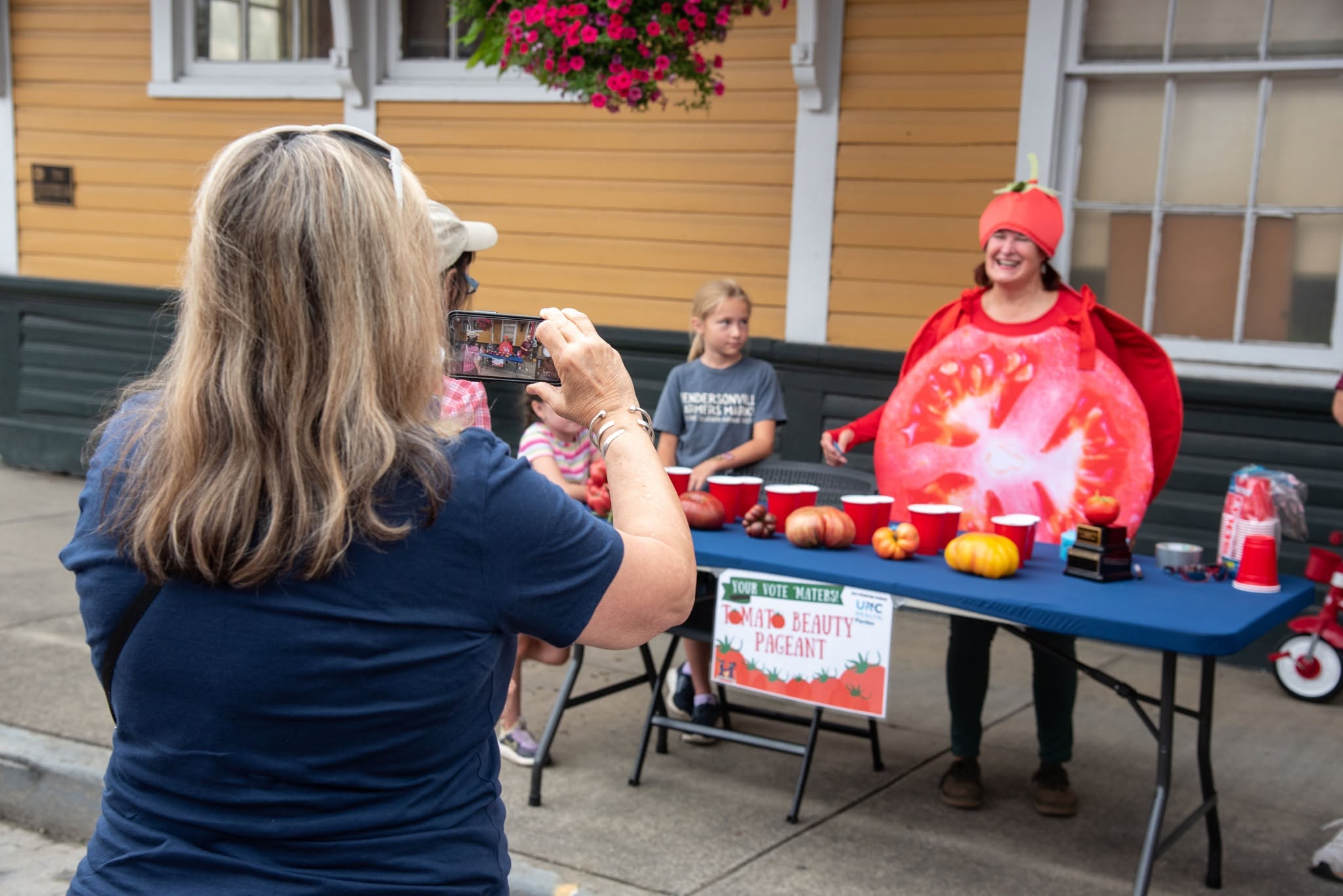 a women in a in a tomato costume getting her picture taken while annoying the winner of a tomato beauty pageant 