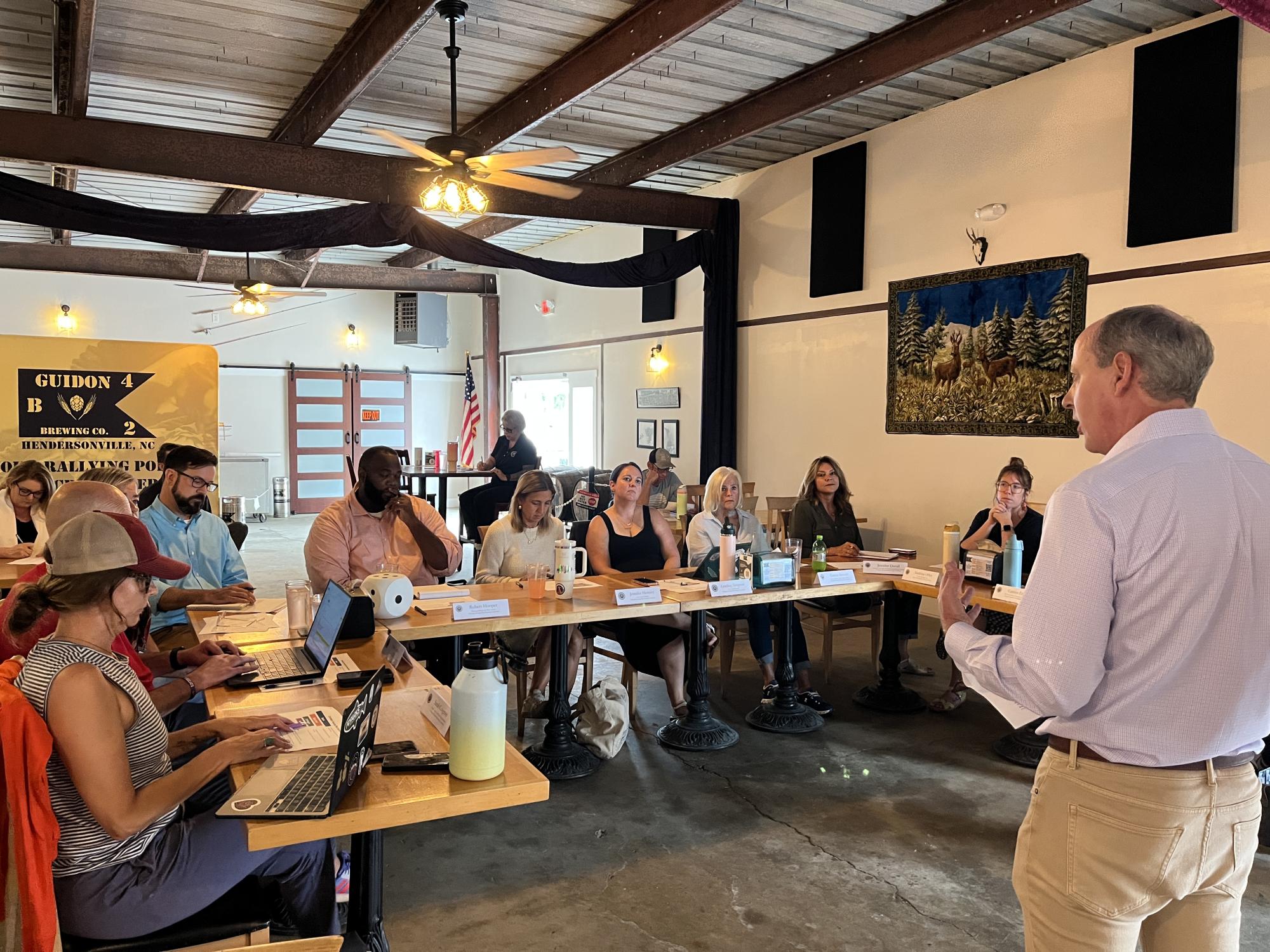 facilitator speaking to a group of committee members seated around a table