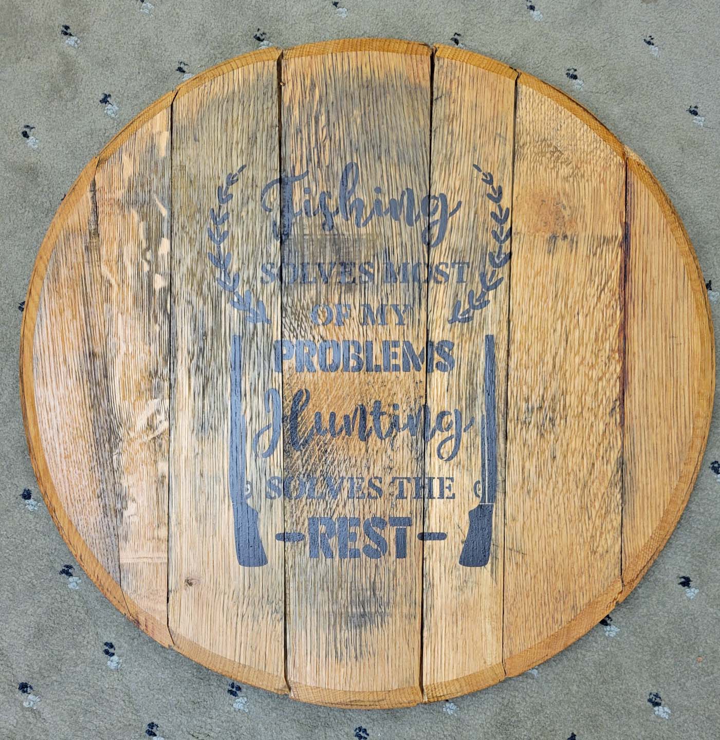 round handmade wooden sign with blue writing with a rifle detailing on both sides of writing