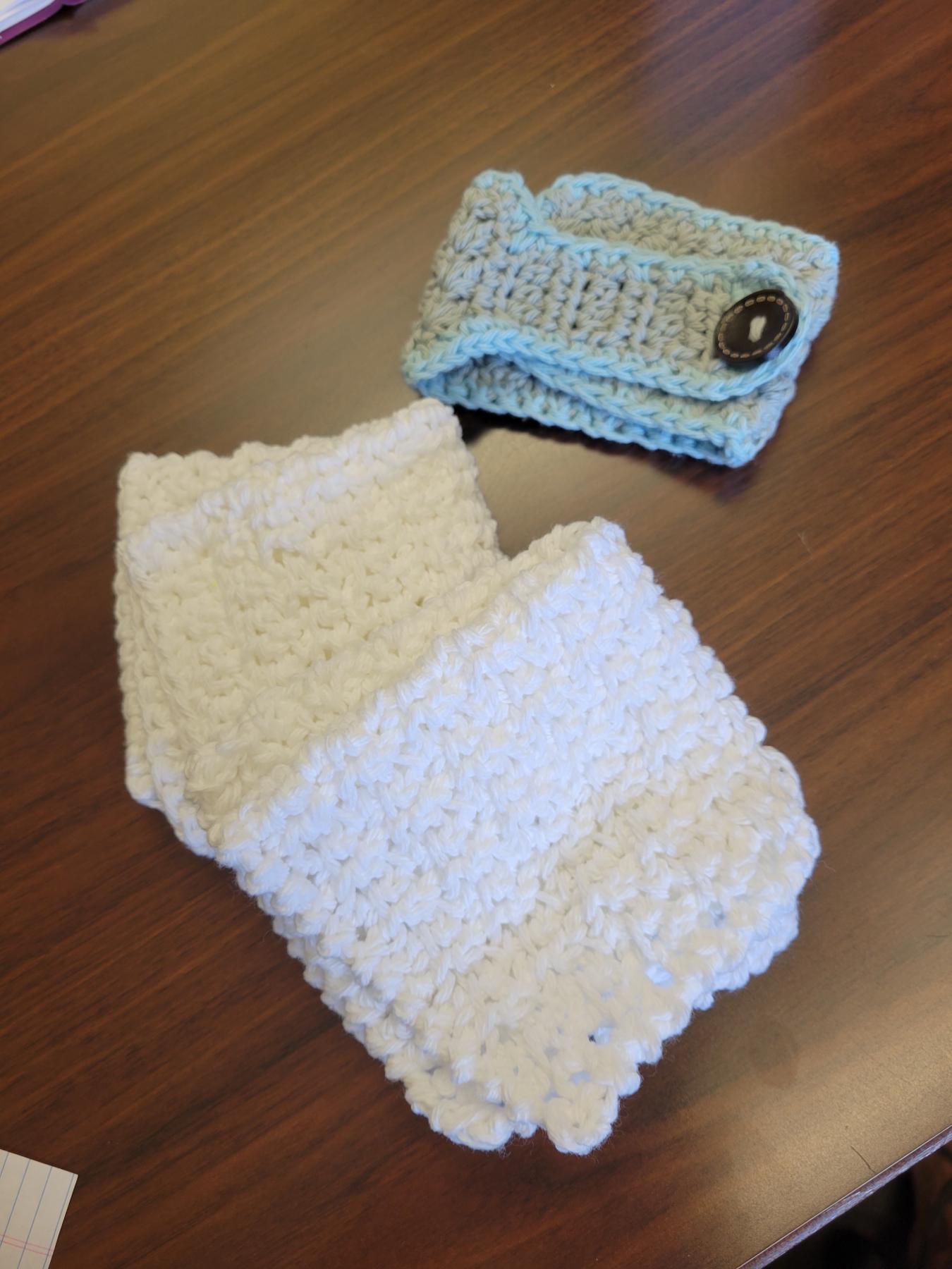 Crocheted light blue cup cozy with brown button and two white crocheted wash cloths 