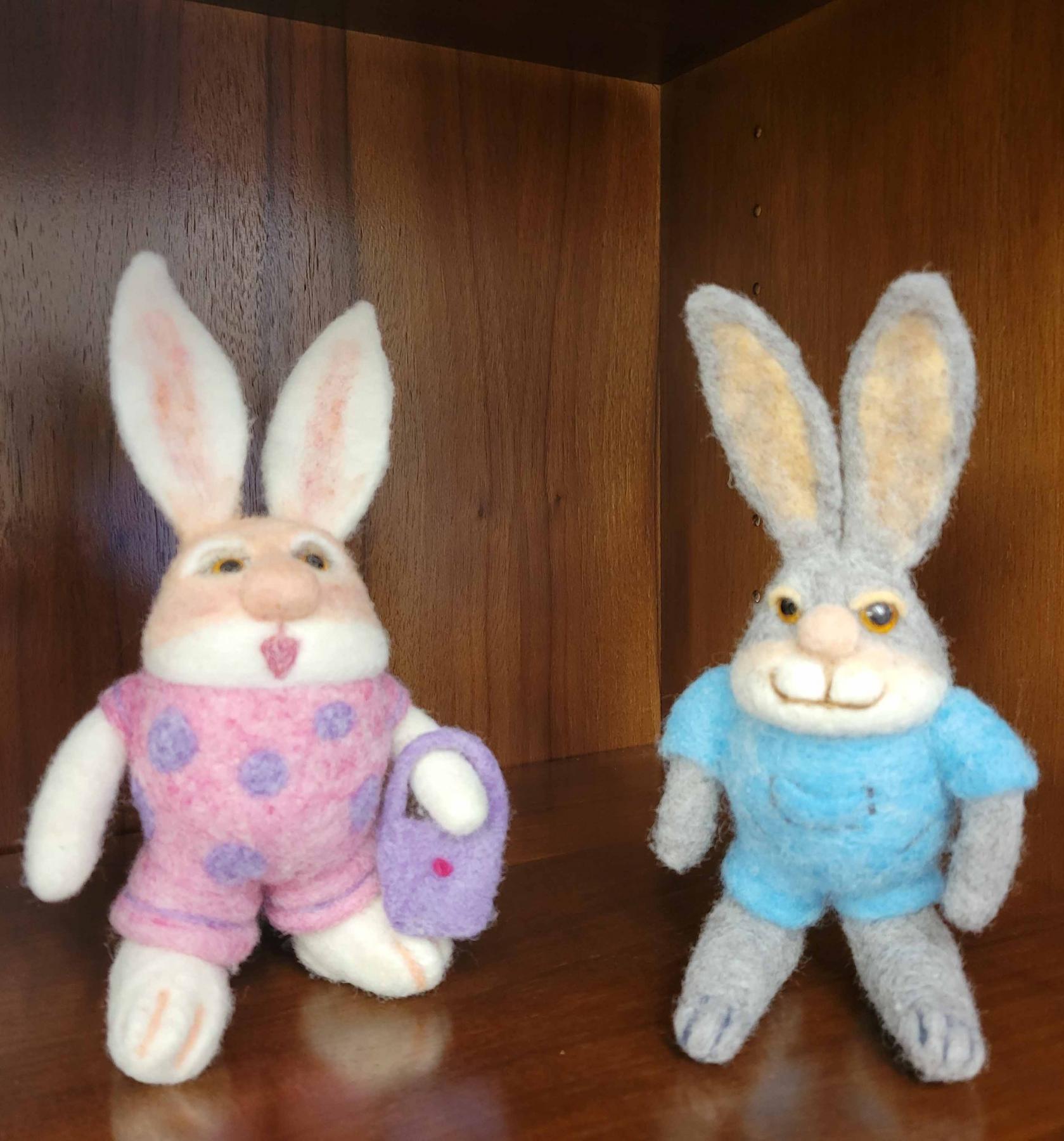 two needle folded bunnies. One with a blue shirt and one with a pink shirt with eggs on it.