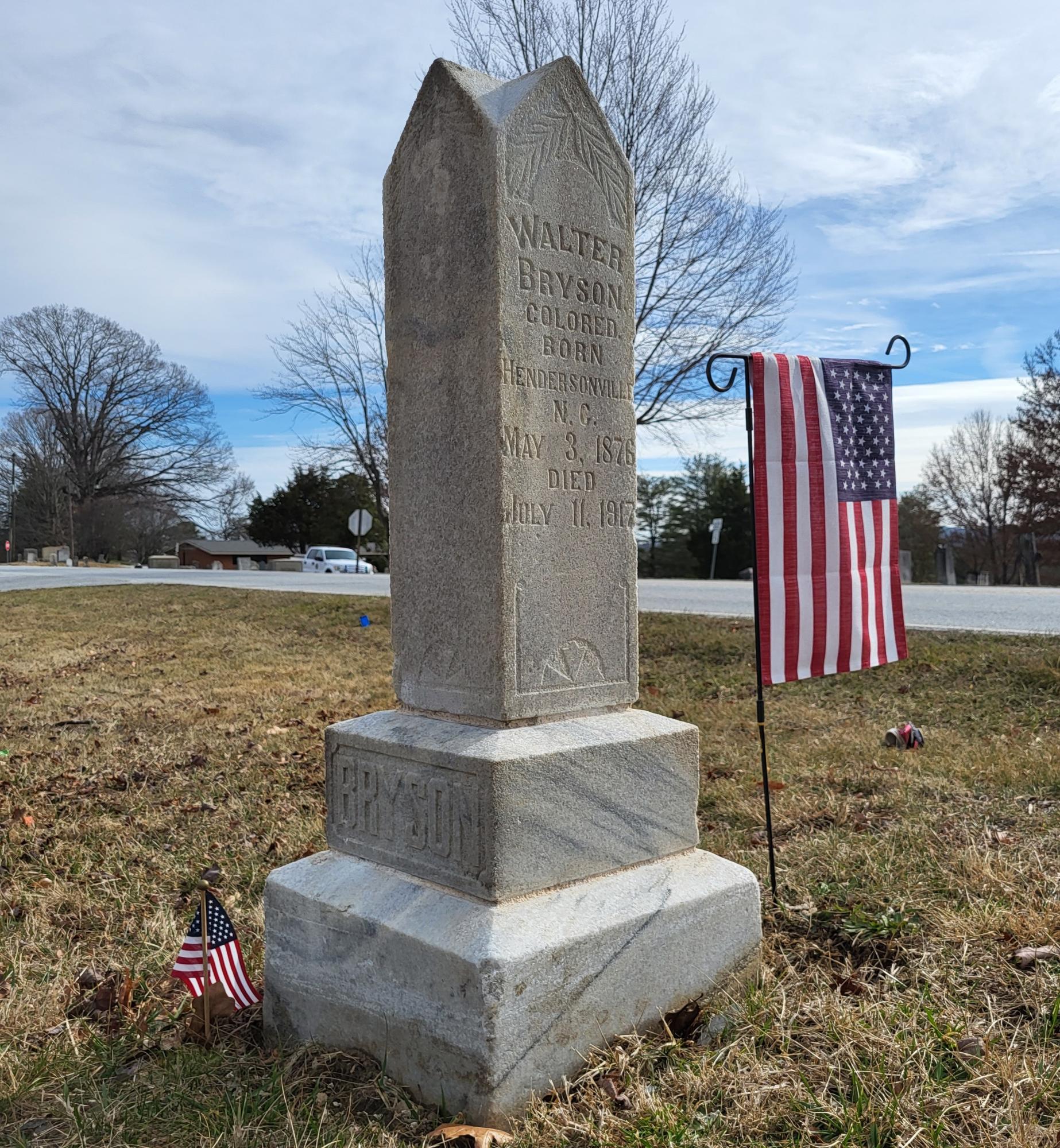 Stone headstone marker in a cemetery, with two small American flags on each side.